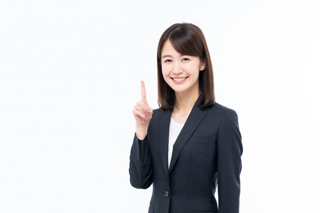 右手の人差し指を上に向けているスーツを着た女性